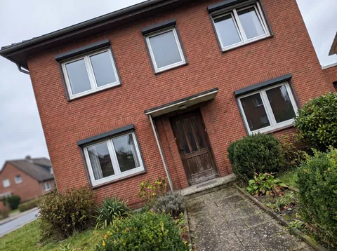 Handyfoto der vorderen Klinkerfassade mit alten Fenstern und Holzhaustür