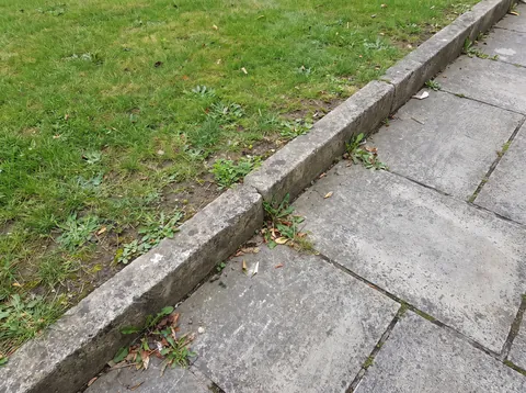 Handyfoto vom Terrassenrand mit Betonplatten und Bordstein als Untergrund für die Pfosten