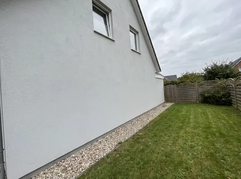 Handyfoto der Hausseite mit Kiesstreifen und Rasen als möglicher Aufstellort der Wärmepumpe